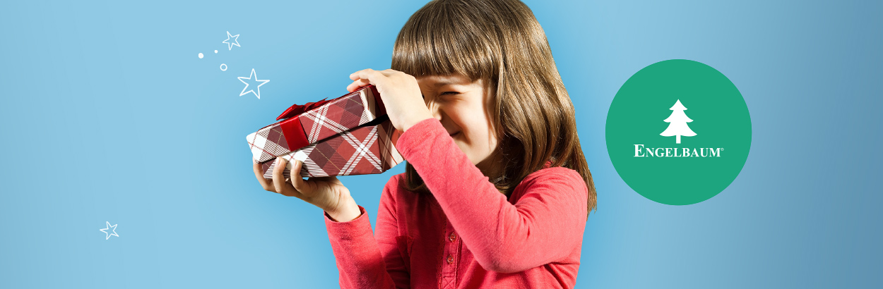Bild eines Mädchens in rotem Shirt und schulterlangen braunen Haaren vor himmelblauem Hintergrund, welches neugierig den Deckel einer rot karierten Geschenkeschachtel mit roter Satinschleife öffnet. Über der Schachtel verteilt schweben weiße illustrierte Sterne in verschiedenen Größen und rechts ein grüner runder Button mit dem weißen Engelbaum Logo in Form einer weißen illustrierten Tanne und dem Schriftzug Engelbaum® mittig darunter.