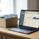 Laptop mit geöffnetem CRM-Dashboard neben einer minimalistischen Visitenkarten-Box auf modernem Schreibtisch im weichen Seitenlicht.