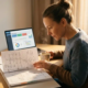 Fachkraft am Schreibtisch studiert Workflow-Diagramme in einem Ordner, ERP-Dashboard auf Laptop im Hintergrund, Kaffeetasse daneben.
