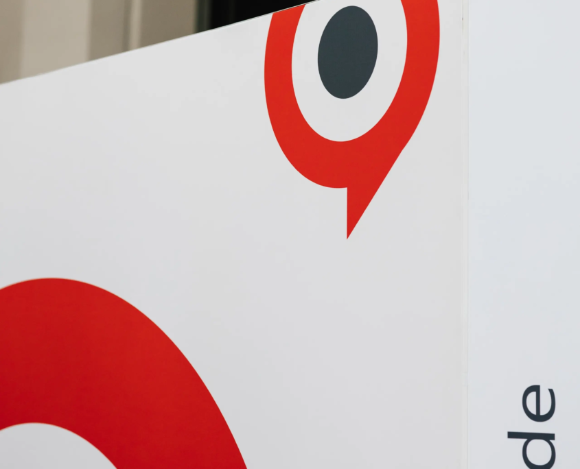 Deitailaufnahme einer weißen Werbesäule mit dem schwarz-rot-grauen Logo-Icon des Customer Centricity Forums 2026, einer Kombination von Sprechblase und Zielscheibe. Seitlich auf der Säule steht die Internetadresse "cas.de" senkrecht von unten nach oben.