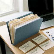 Geöffnete Kundenakte auf modernem Büroschreibtisch mit beschrifteten Karteikarten, Kontaktbogen und Laptop im Hintergrund.