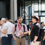 Aufnahme von Besuchern des Customer Centricity Forums 2026 beim Smalltalk und Snacken im Foyer des ZKM, Zentrum für Kunst und Medien in Karlsruhe. Zwischen den Besuchern flattern zwei kleine rot-schwarze Schmetterlinge herum.
